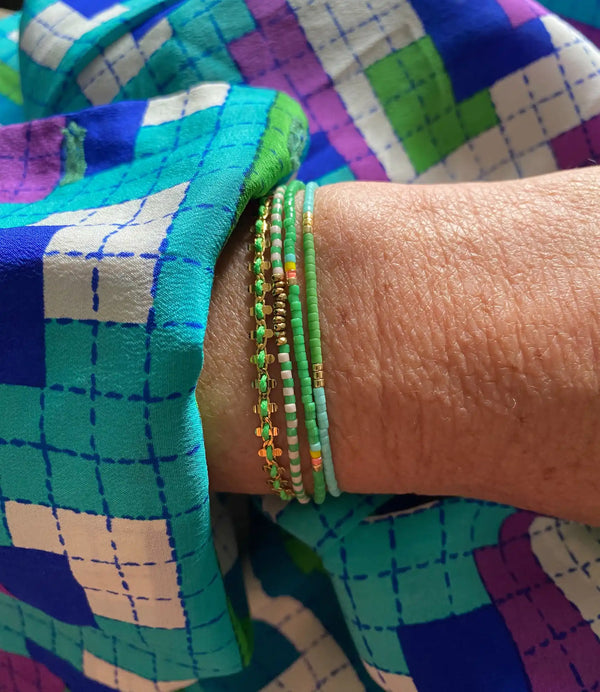 Le poignet d'une personne orné d'une pile de bracelets verts et dorés.