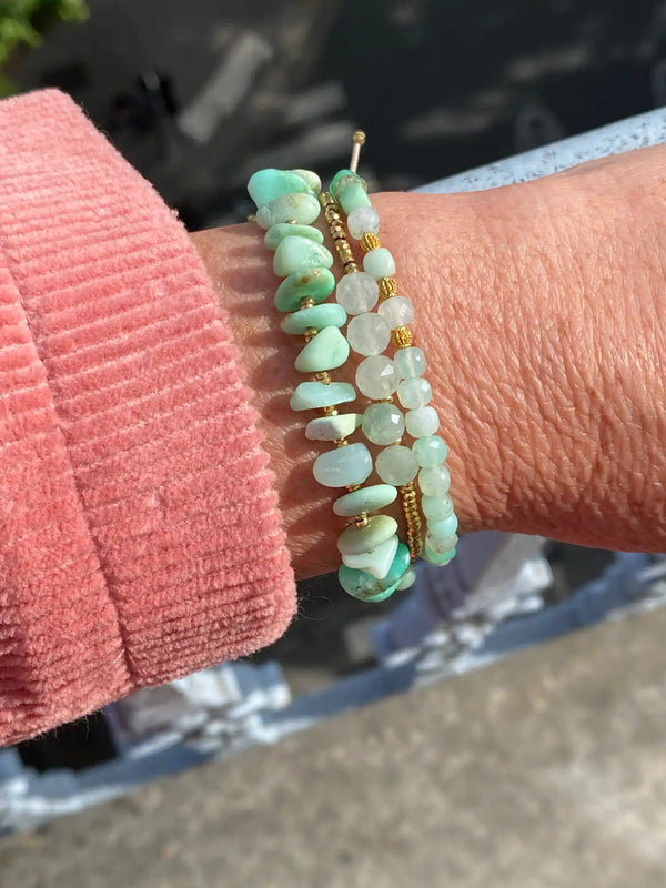Le poignet d'une personne orné de trois bracelets comportant diverses perles vertes et de couleurs claires, avec des perles séparatrices en or sur deux d'entre eux.